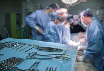 Closeup of surgical tools on table and team of surgery doctors operating a patient in hospital room.